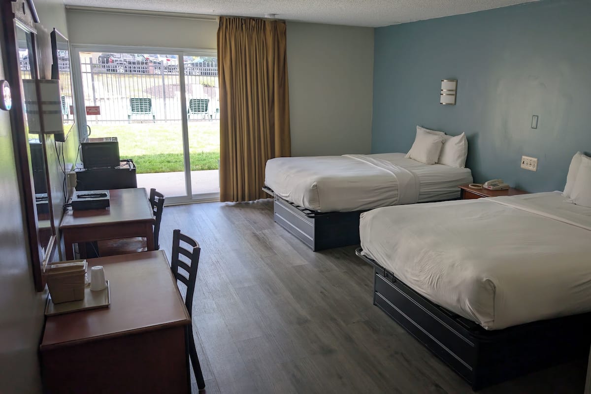 Habitació d'hotel amb dos llits, un escriptori amb cadira, un telèfon i vista exterior per una porta corredissa.