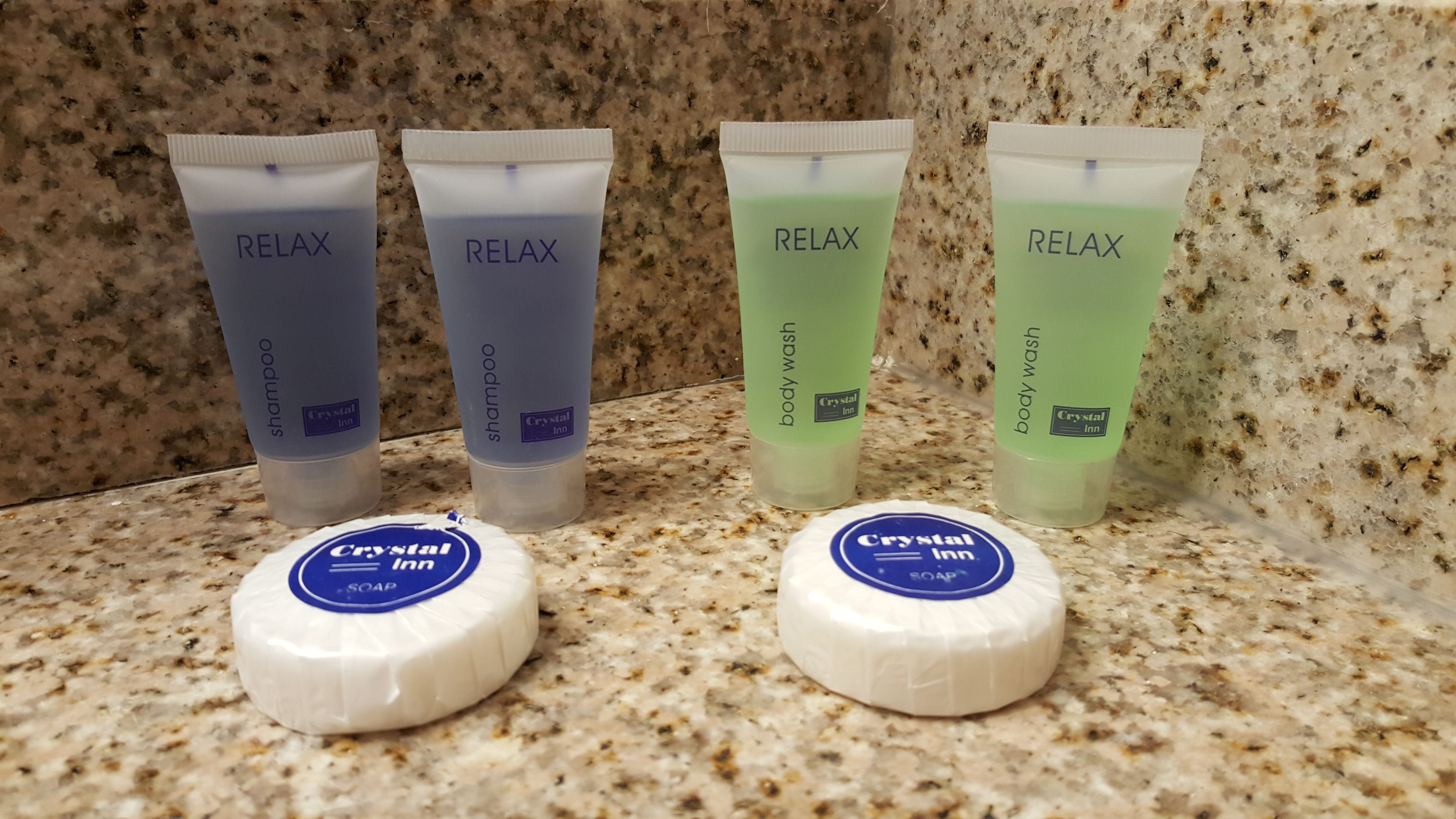 Vier Flaschen Crystal Inn Duschgel und Shampoo sowie zwei Seifenstücke von Crystal Inn auf einer Granitplatte.