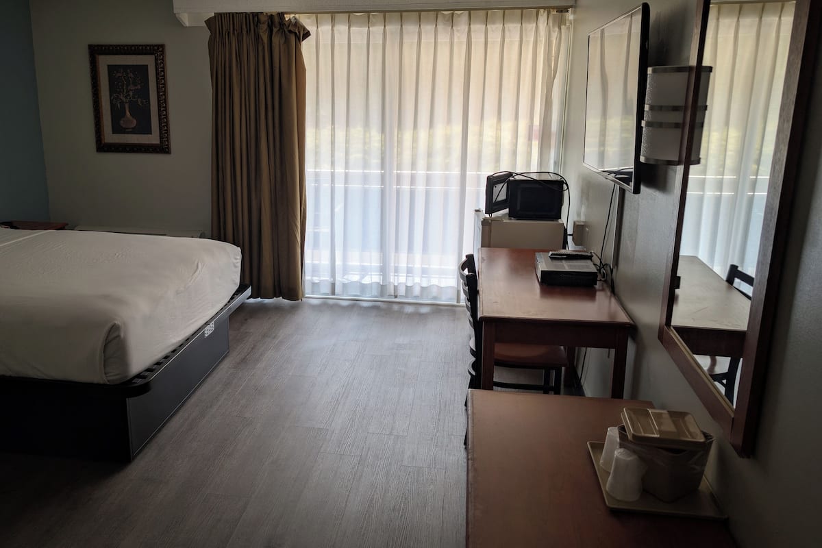 Habitació d'hotel amb llit, escriptori, cadira, televisió i finestra amb cortines.
