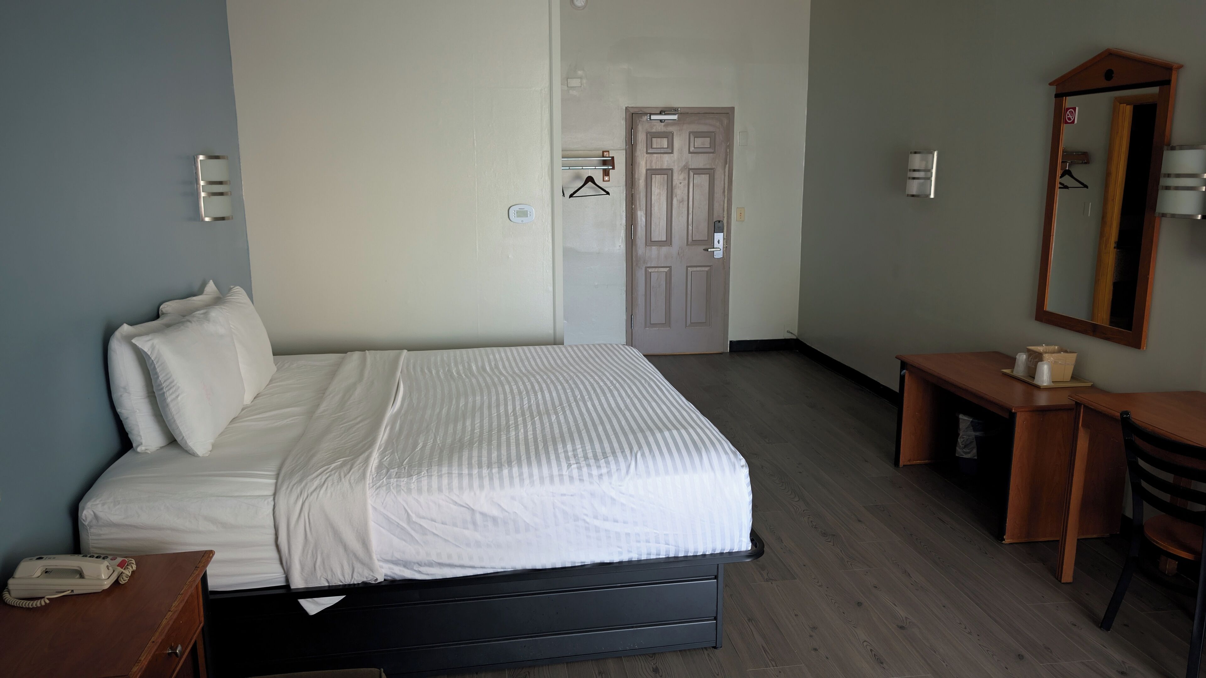 A hotel room with a bed, bedside table, chair, and a mirror.