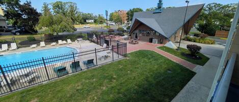 A residential area with a swimming pool, a fenced patio with lounge chairs, and a building with a unique roof design.