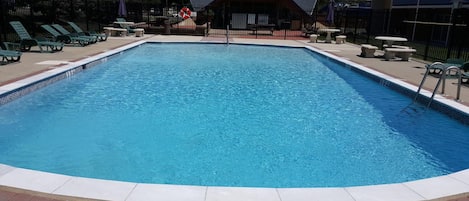 A rectangular swimming pool with a no diving sign at the edge, surrounded by lounge chairs and tables.