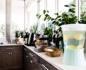 A kitchen with dark cabinets, a white countertop, and various items including a coffee maker, a basket, and a large pitcher. - Crystal Inn Eatontown (Eatontown)