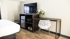 Habitación de hotel con cama, escritorio, televisor de pantalla plana, microondas y una silla blanca.