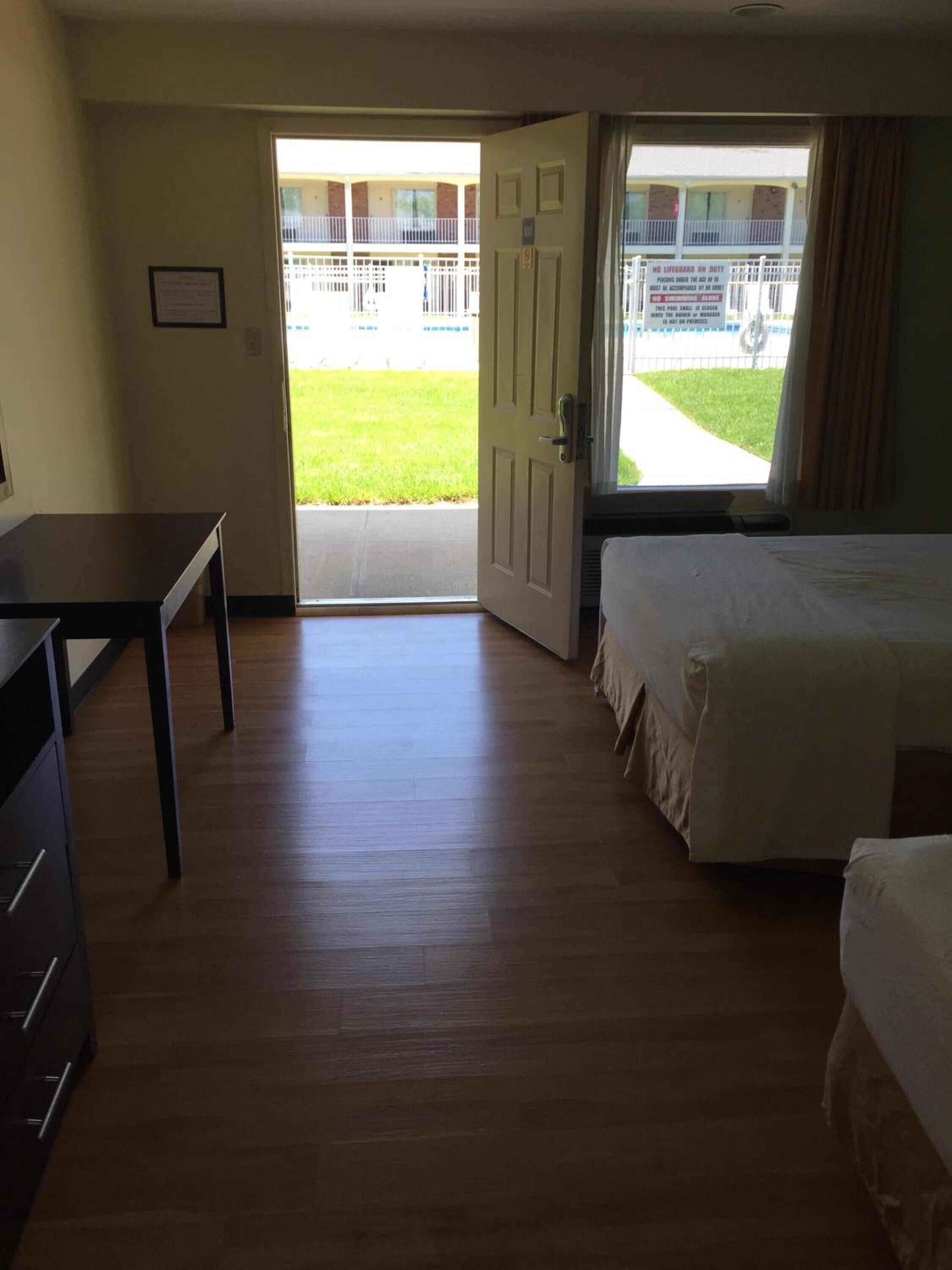 A hotel room with a wooden floor, a desk, a bed, and a door leading to a balcony.