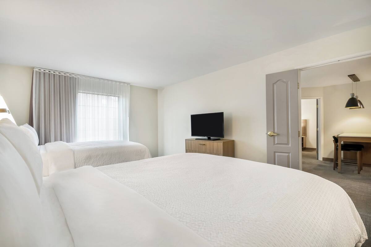 A hotel room with two beds, a television, a desk, and a chair.