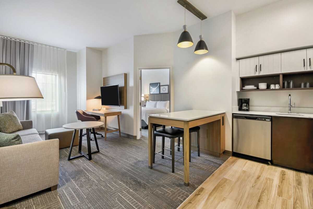 A modern hotel room with a living area, dining table, and kitchenette.