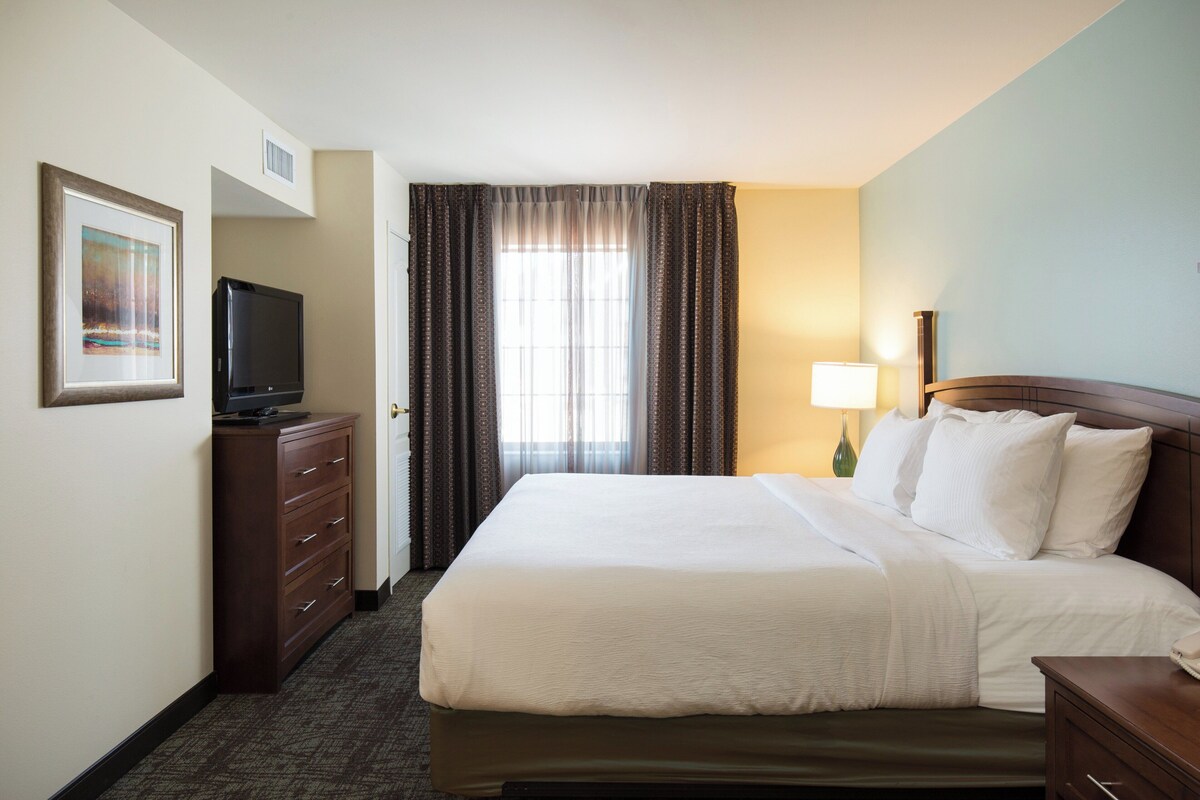 A hotel room with a bed, a dresser, a television, and a window with curtains.