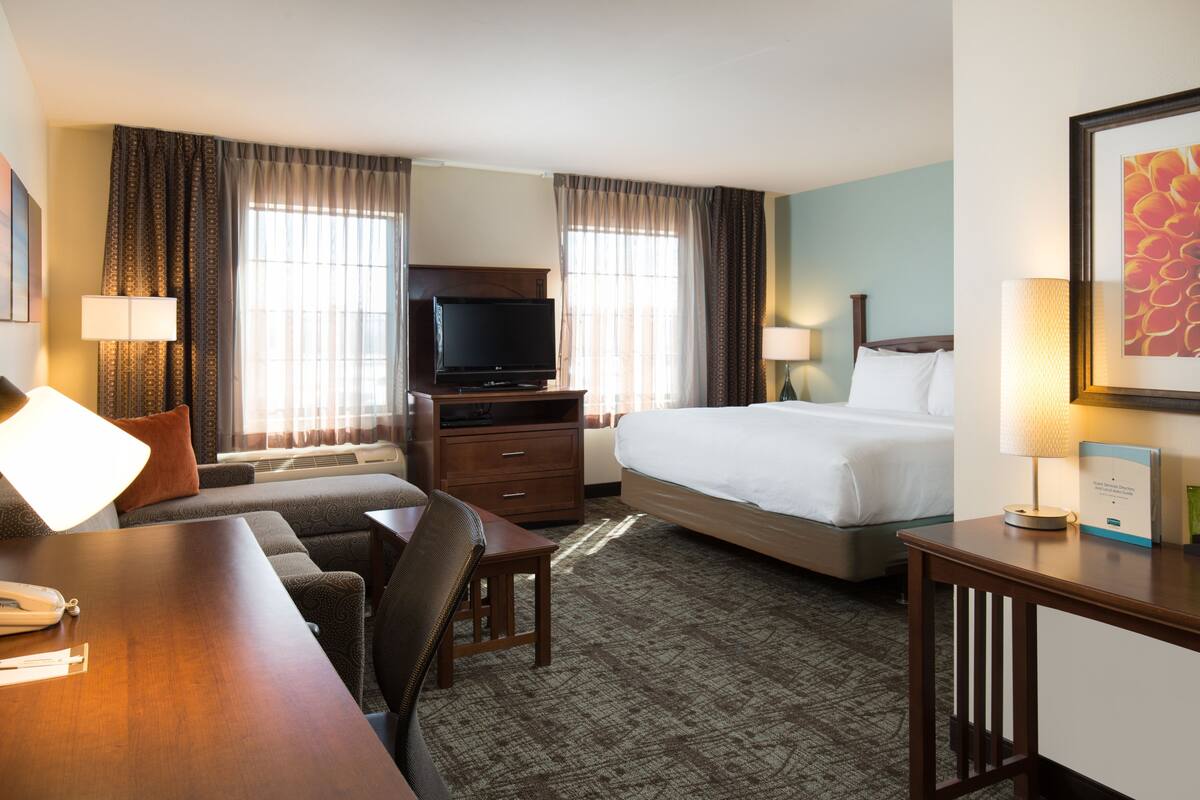 A hotel room with a bed, a desk with a lamp, a television, and a sofa.