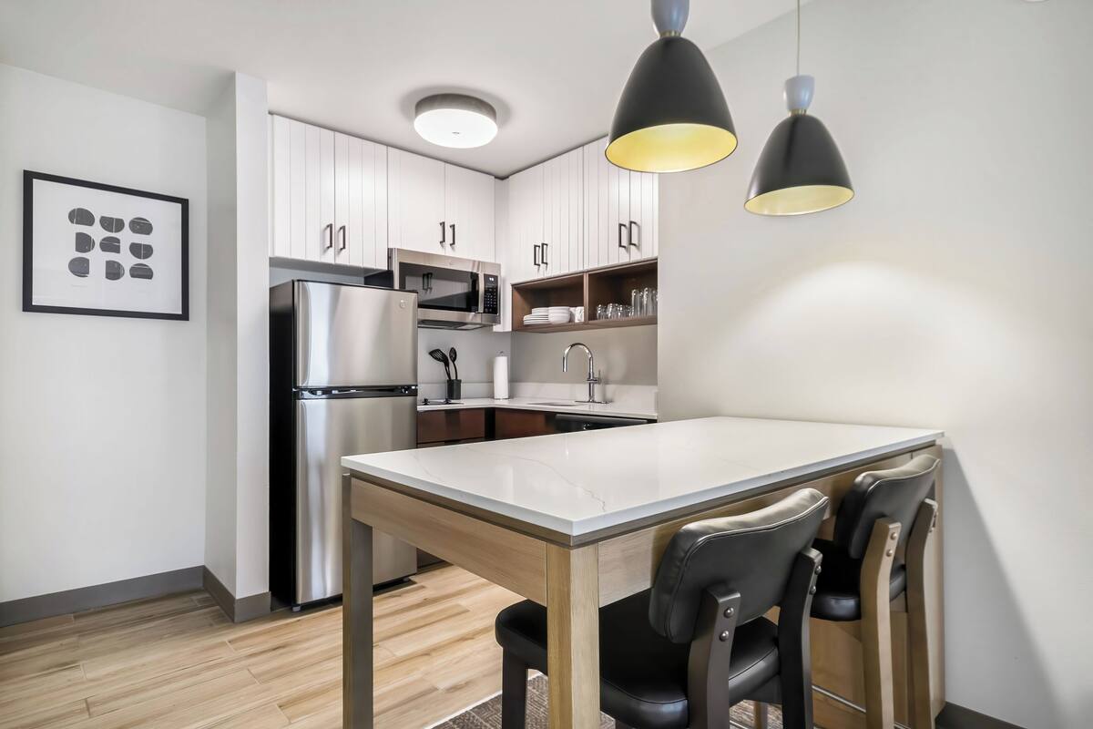 A modern kitchen with white cabinets, stainless steel appliances, a wooden dining table, and black chairs.