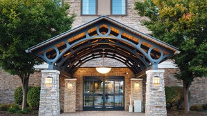 A building entrance with a stone facade, a wooden archway, and a glass door. - Staybridge Suites Toledo - Maumee by IHG (Maumee)