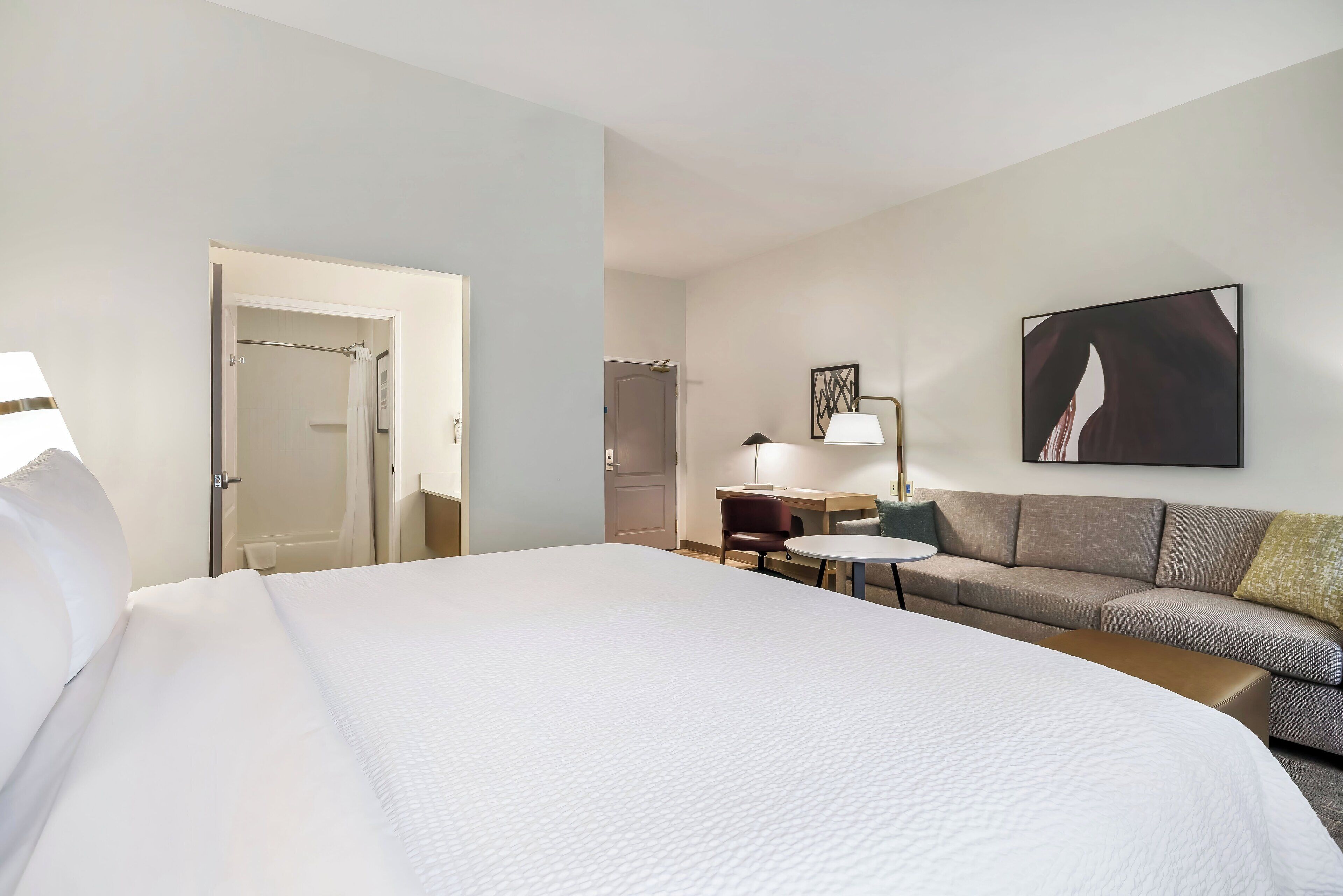 Une chambre d’hôtel avec un grand lit, un canapé, une petite table, une lampe et un tableau au mur.
