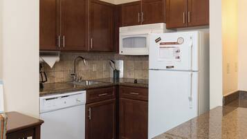 A kitchen with wooden cabinets, a microwave, a refrigerator, a dishwasher, and granite countertops.