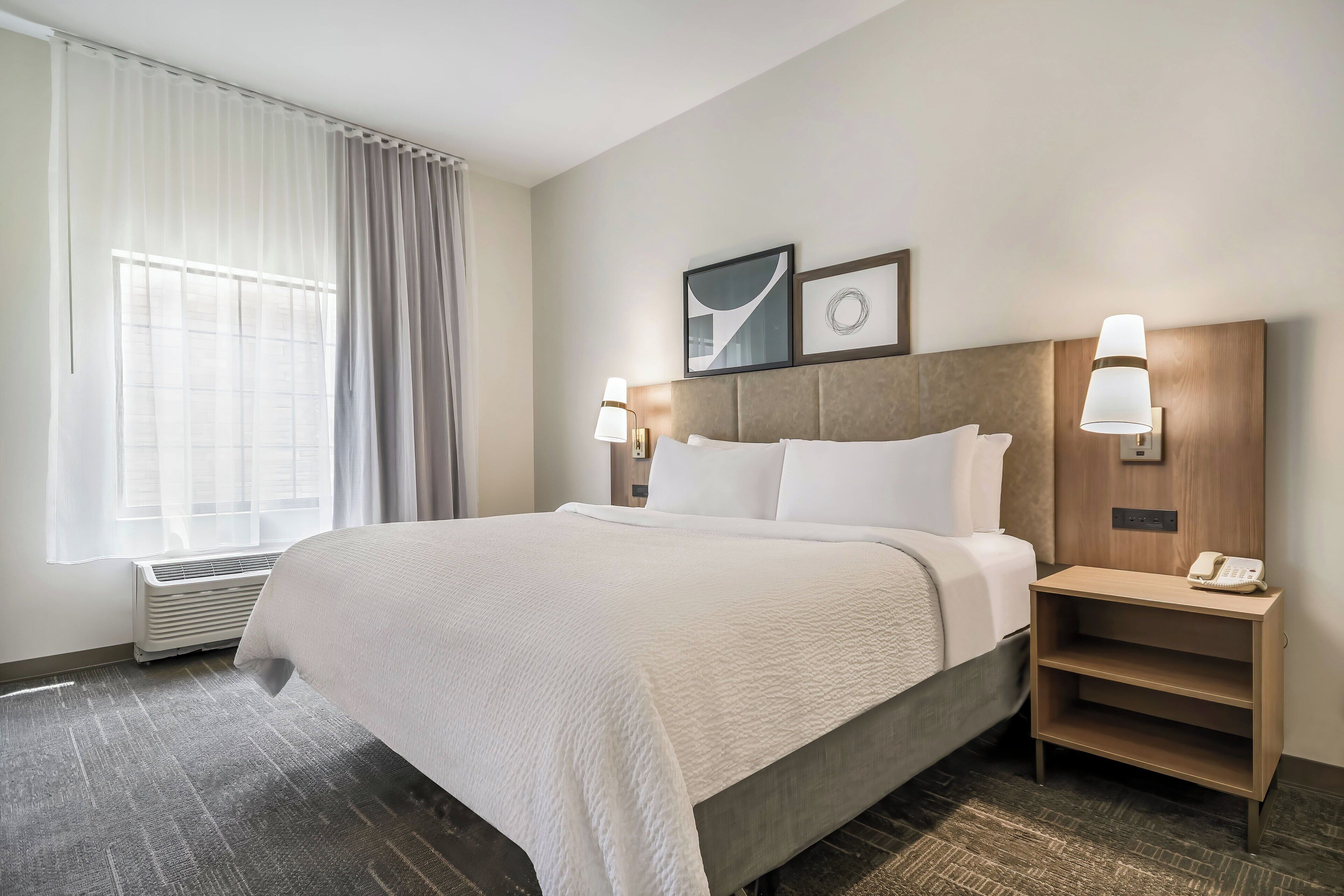 A hotel room with a large bed, a bedside table with a lamp, and a wall-mounted phone.