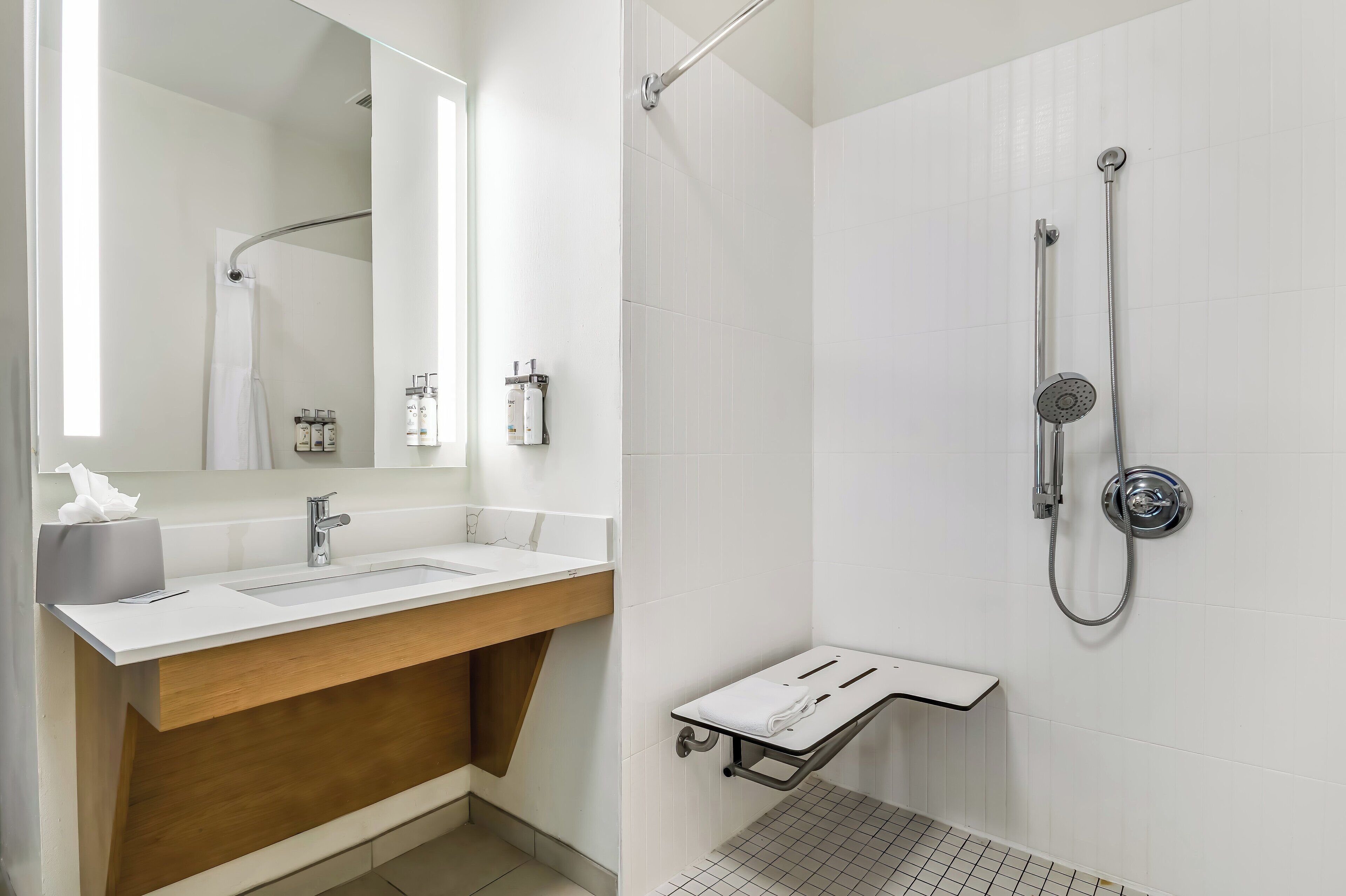 A modern bathroom with a white sink, wooden vanity, a large mirror, and a shower with a handheld showerhead.