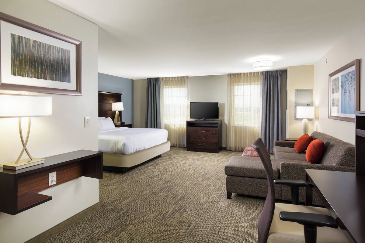 A hotel room with a bed, a desk, a television, a sofa, and a chair.