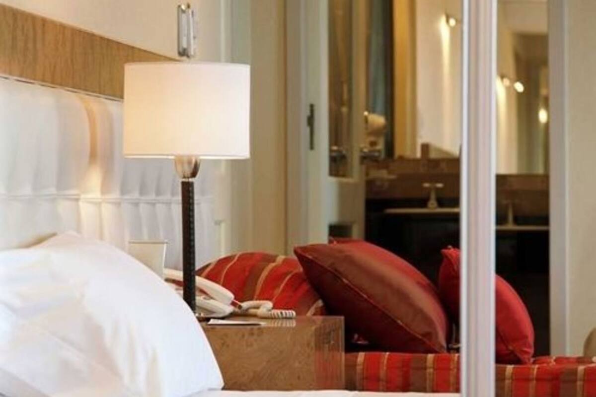 Ein Hotelzimmer mit einem Bett, einer Nachttischlampe, einem Telefon und einem roten karierten Kissen.