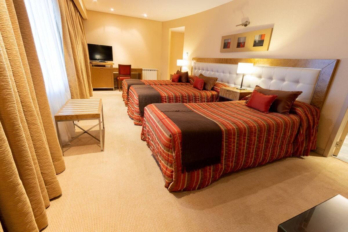 Ein Hotelzimmer mit zwei Betten, einem Schreibtisch, einem Fernseher und Blick auf die Stadt.