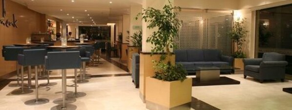 A hotel lobby with a reception desk, bar area, seating with sofas and chairs, and potted plants.