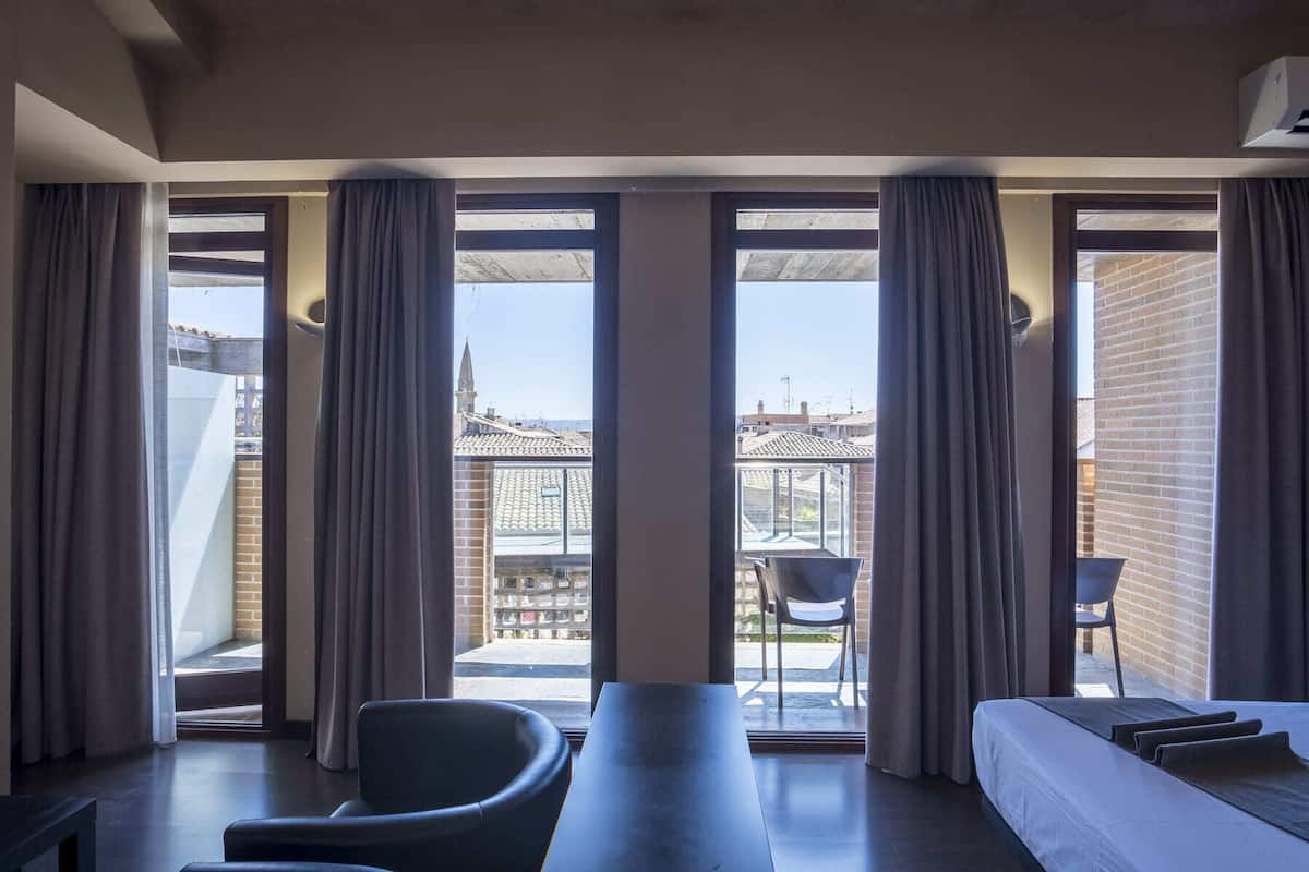 A modern hotel room with a large balcony, a sofa, a dining table, and a chair.
