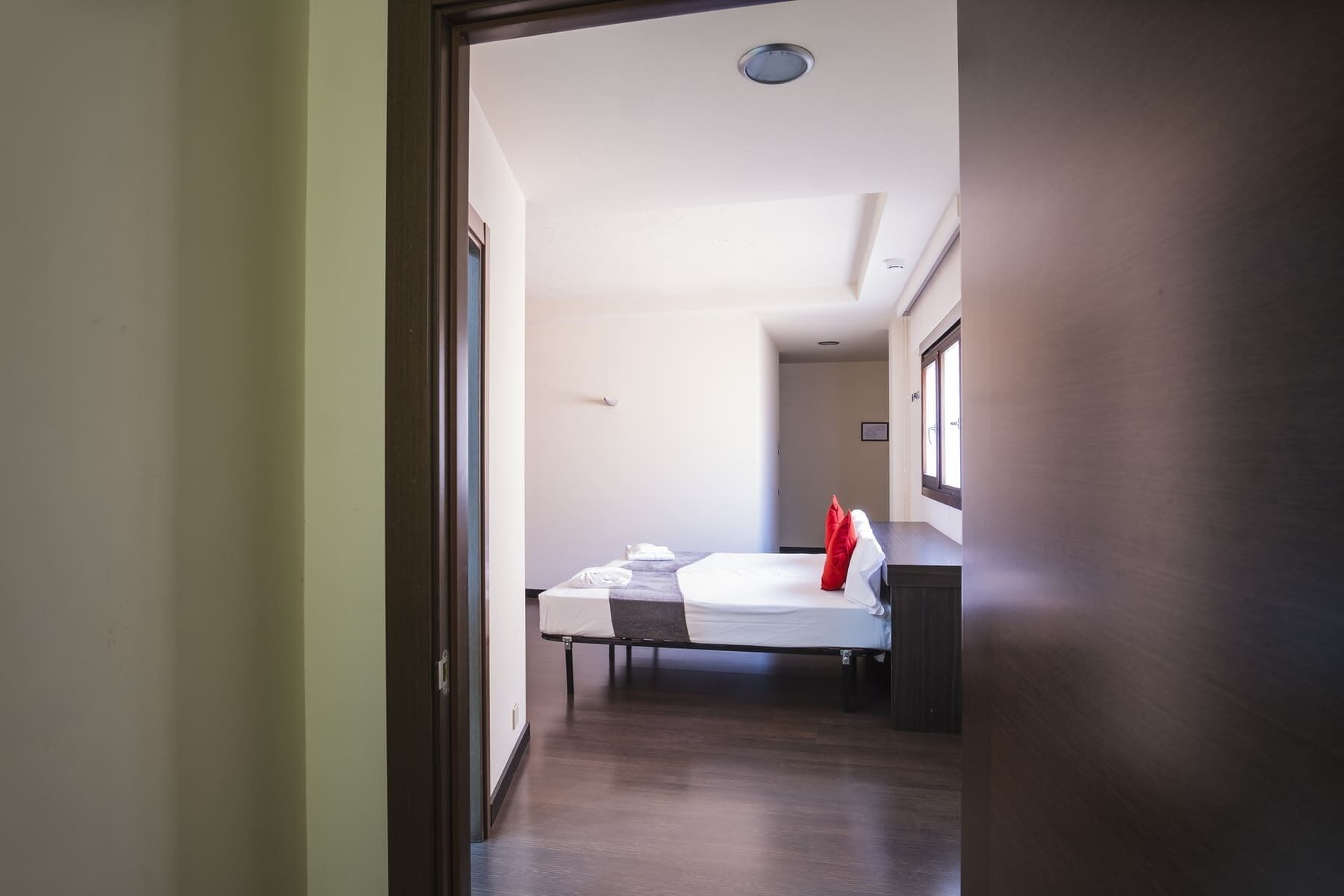 A hotel room with a bed, a window, and a door leading to another room.
