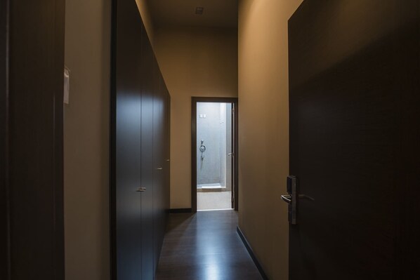 Un pasillo estrecho con puertas de madera oscura a ambos lados, que conduce a una habitación con un ventanal grande.