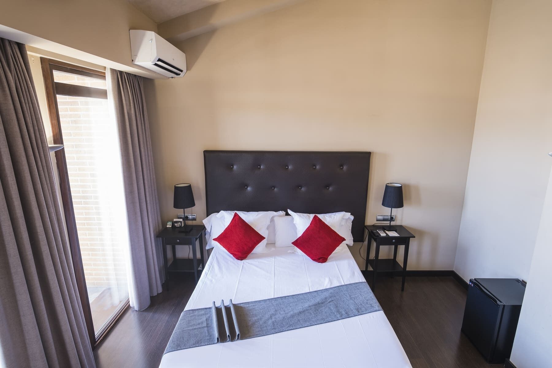 Une chambre d’hôtel avec un grand lit, deux tables de chevet, un climatiseur et une poubelle.