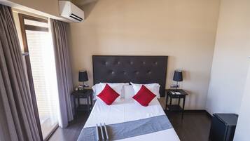 Une chambre d’hôtel avec un grand lit, deux tables de chevet, un climatiseur et une poubelle.