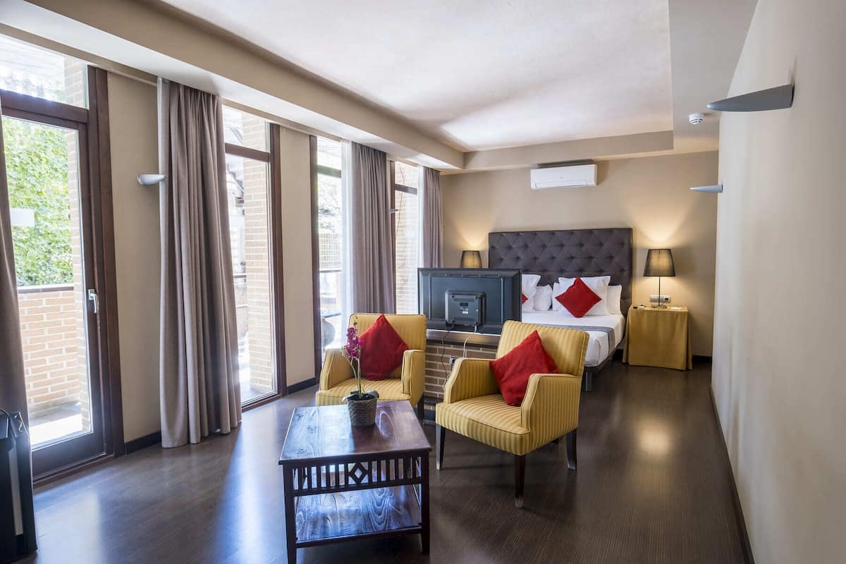 A hotel room with a bed, a television, a desk, two chairs, and a window with curtains.