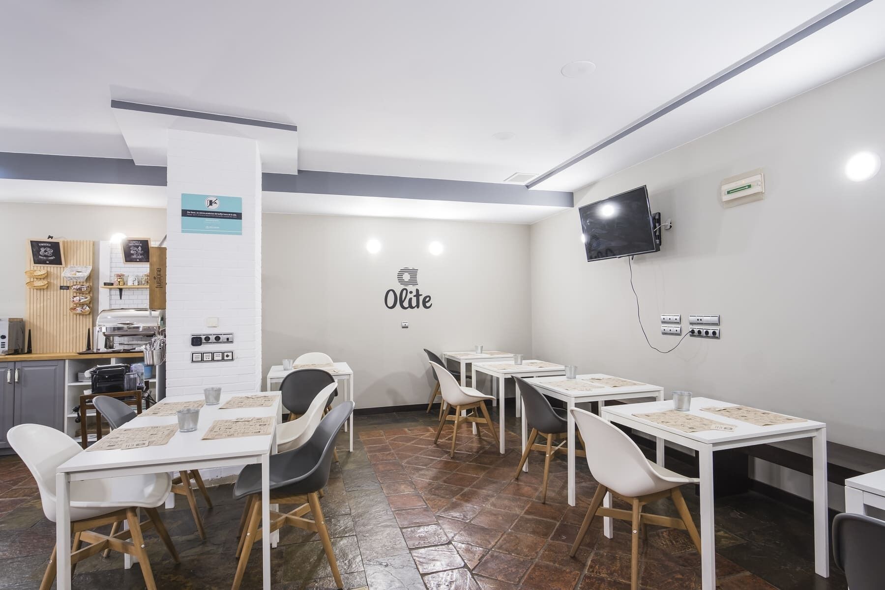 Een modern café met witte tafels en stoelen, een koffieapparaat en een menubord.