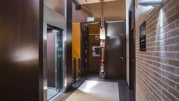 Un couloir avec un ascenseur, un extincteur et un dispositif de déclenchement d’alarme incendie.