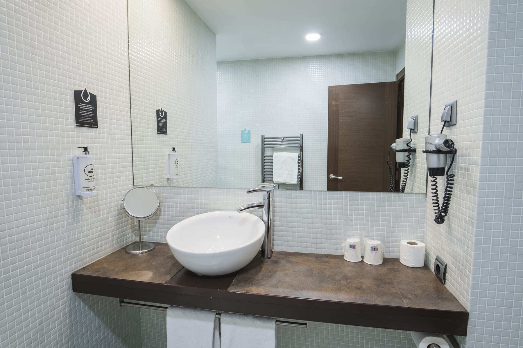 Un baño moderno con un lavamanos grande, un espejo, un perchero para toallas y un secador de pelo.