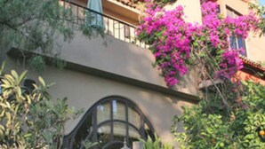 A building with a stone wall, potted plants, and a balcony with pink flowers. - Casa Cordelli (San Miguel de Allende)