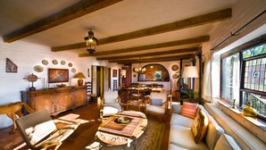 A spacious living room with a wooden floor, a sofa, a coffee table, and a dining area with chairs and a table. - Casa Cordelli (San Miguel de Allende)