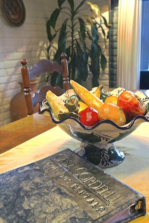 A bowl of bread and fruit on a table with a book titled "CASA CORDELLI LUXURIOUS RENTALS" in front.