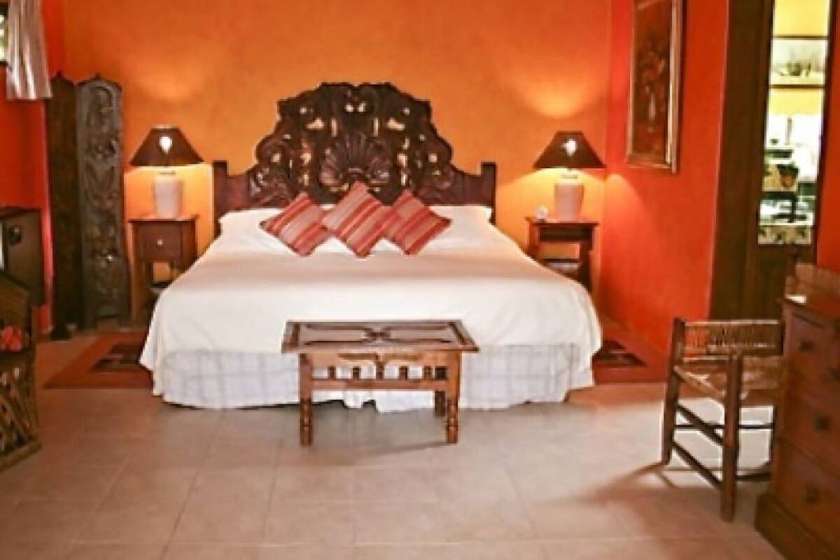 Une chambre à coucher avec un grand lit, deux tables de chevet avec des lampes, une petite table en bois, une chaise et une commode.