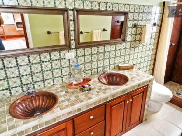 A bathroom with a tiled backsplash, two sinks, a mirror, and a toilet.