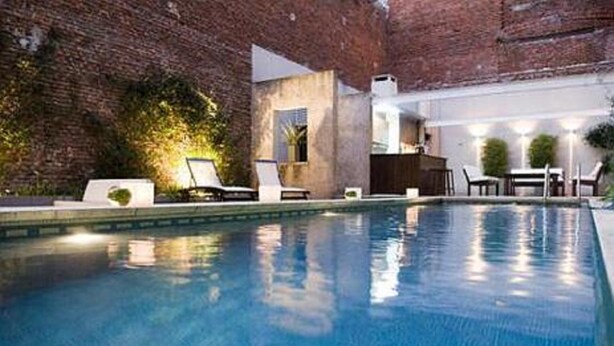 An indoor swimming pool with lounge chairs and a brick wall backdrop. - Ribera Sur Hotel (Buenos Aires)