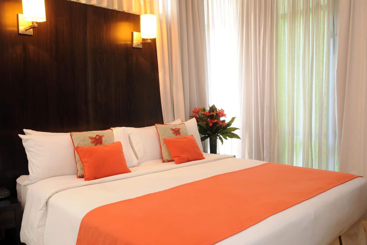 A hotel room with a large bed, white bedding, and orange accents. There are two wall-mounted lights above the bed and a vase with flowers on the nightstand.