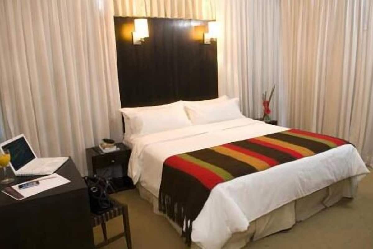 A hotel room with a large bed, a desk with a laptop, and a nightstand with a lamp.