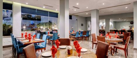 A restaurant with round tables, blue chairs, and red napkins.