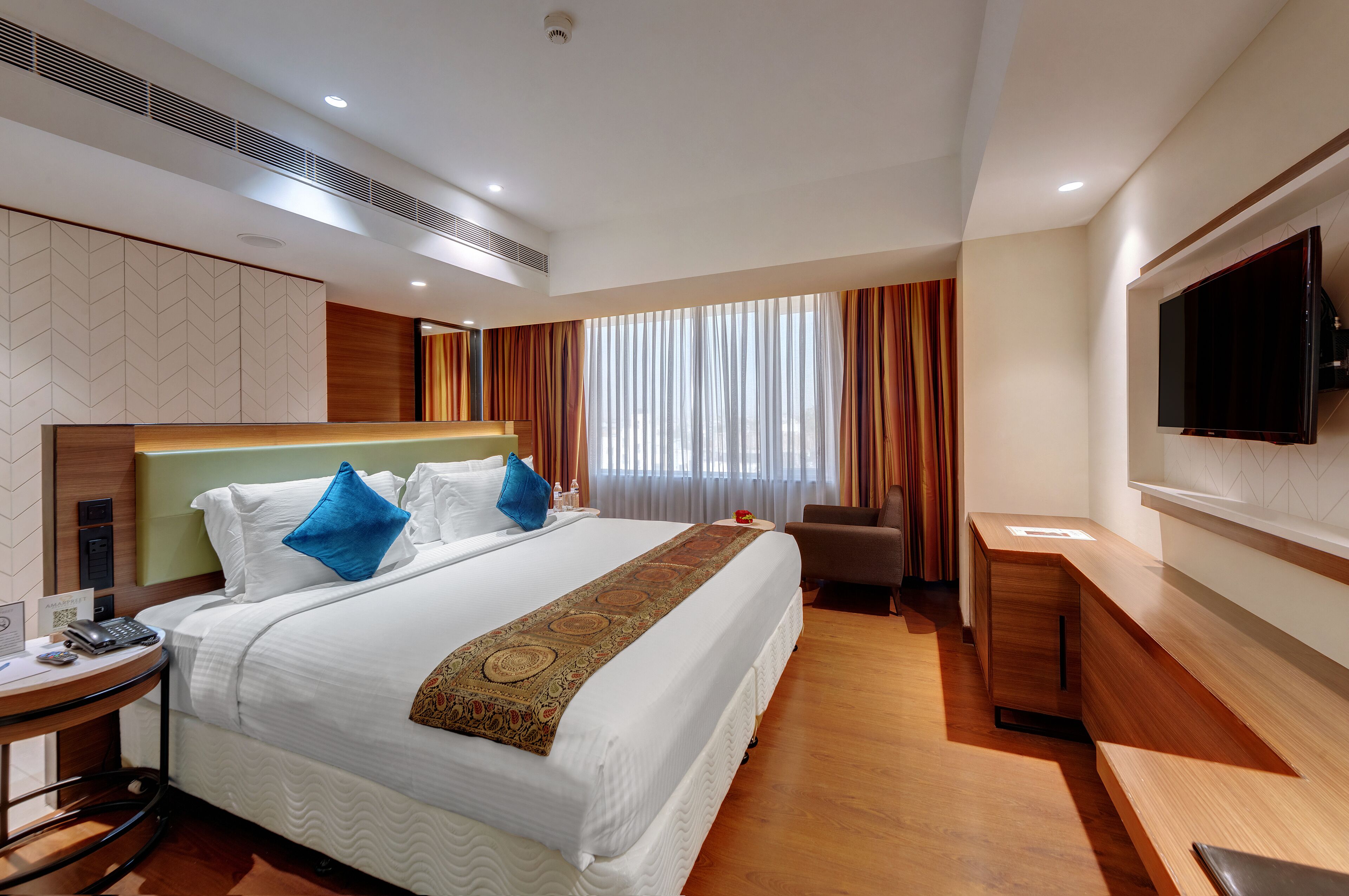 A hotel room with a large bed, a desk, a chair, a TV, and a window with curtains.