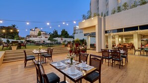 An outdoor dining area with tables set for two, surrounded by wooden chairs and a string of lights. - Amarpreet, Chhatrapati Sambhajinagar - AM Hotel Kollection (Chhatrapati Sambhajinagar)