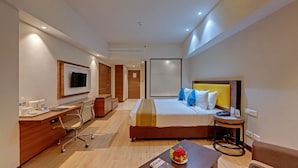 A modern hotel room with a bed, desk, chair, TV, and a small table with a magazine and flowers. - Amarpreet, Chhatrapati Sambhajinagar - AM Hotel Kollection (Chhatrapati Sambhajinagar)