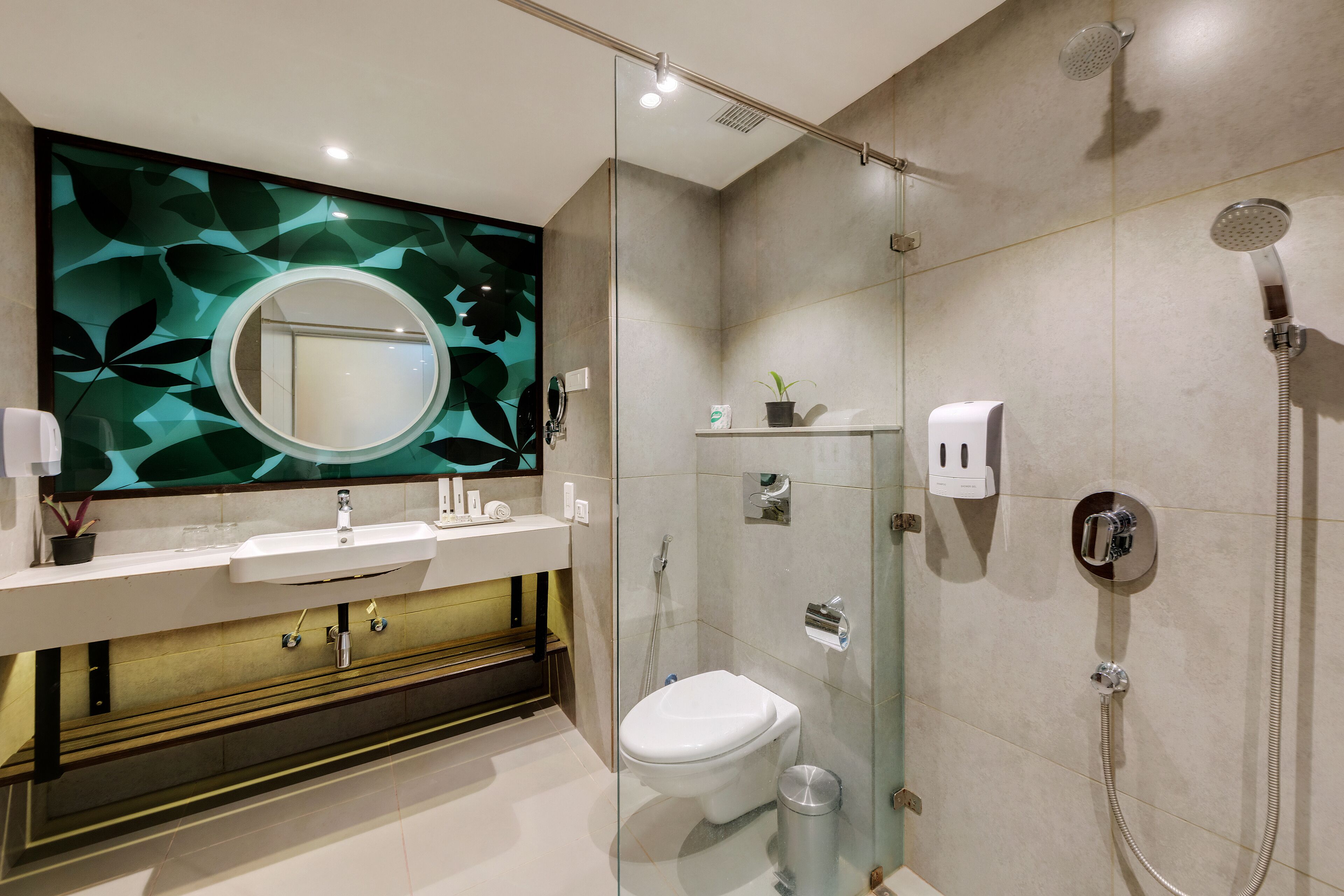 Un bagno moderno con doccia vetrata, lavandino bianco e un ampio specchio con pannello decorato a motivi vegetali.