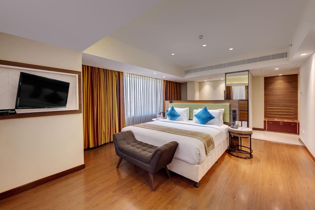 A hotel room with a large bed, a TV mounted on the wall, a small seating area, and a wooden floor.