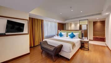 A hotel room with a large bed, a TV mounted on the wall, a small seating area, and a wooden floor.