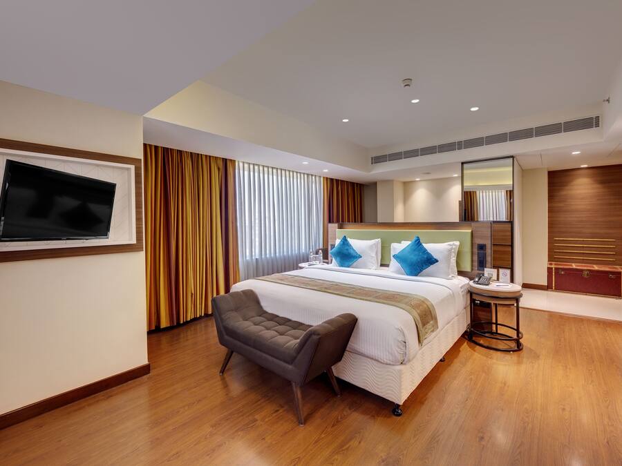 A hotel room with a large bed, a TV mounted on the wall, a small seating area, and a wooden floor.