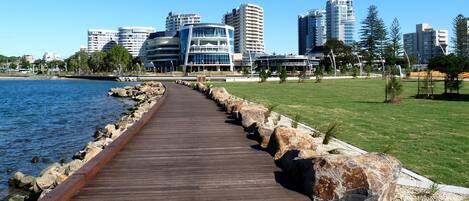 A wooden boardwalk along a waterfront with modern buildings in the background.