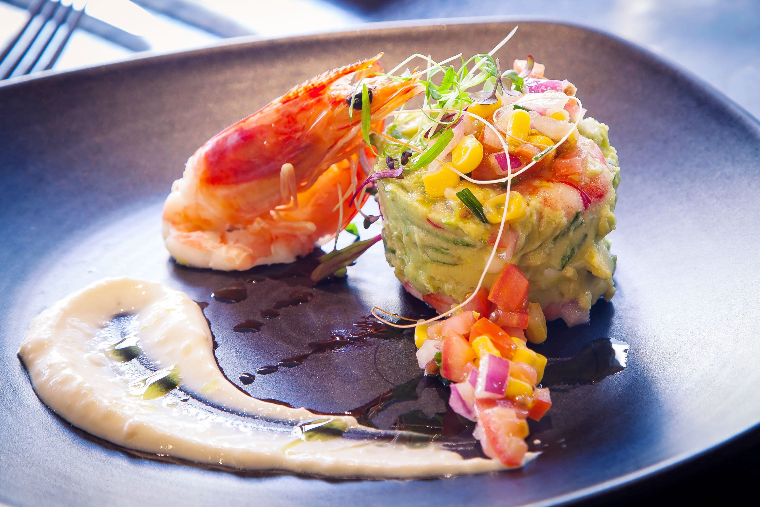 A plate with a shrimp and avocado salad, garnished with microgreens and a drizzle of sauce.